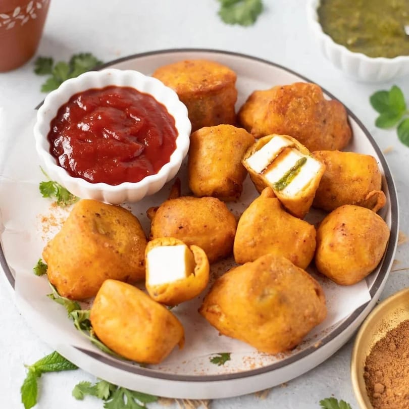 Golden-fried paneer pakoras with ketchup and green chutney, garnished with fresh mint and cilantro.