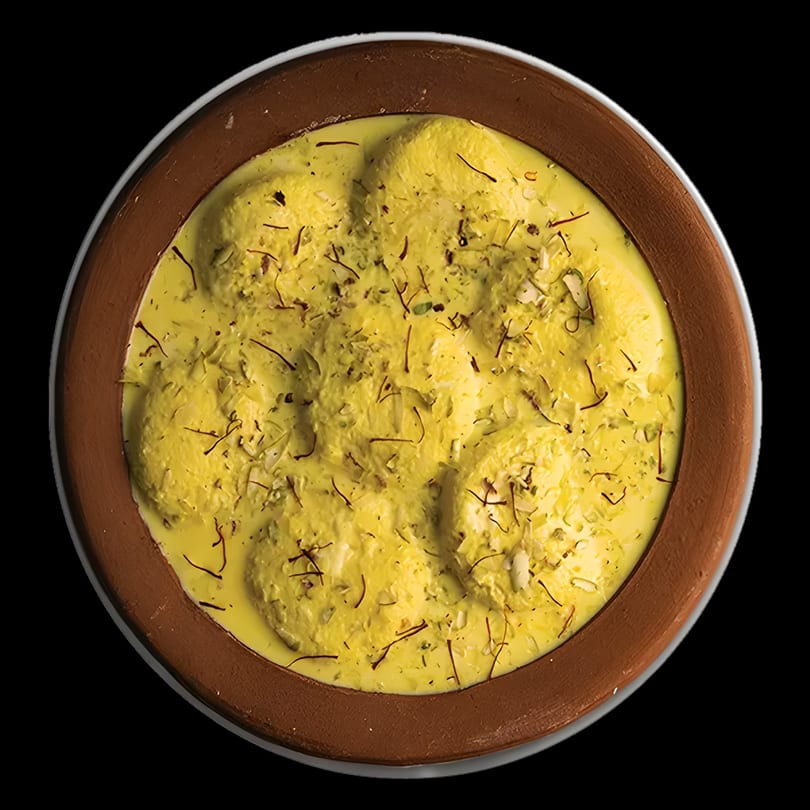 Overhead view of Rasmalai, an Indian dessert, in a brown bowl, garnished with saffron and nuts.